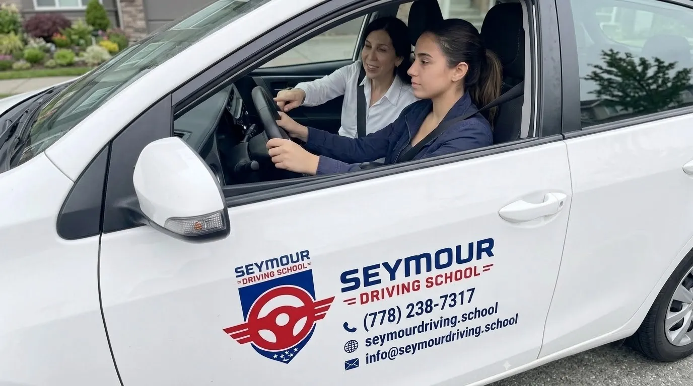 An instructor in the passenger seat guides the steering wheel while a student drives a white Seymour Driving School car.